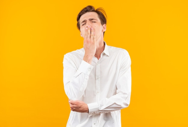 yawning young handsome guy wearing white shirt covered mouth with hand isolated on orange wall