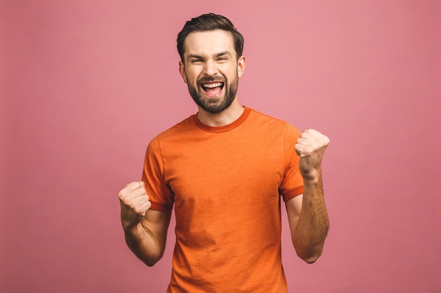 Yeah! Happy winner! Happy young handsome man gesturing and keeping mouth open while standing against pink wall.