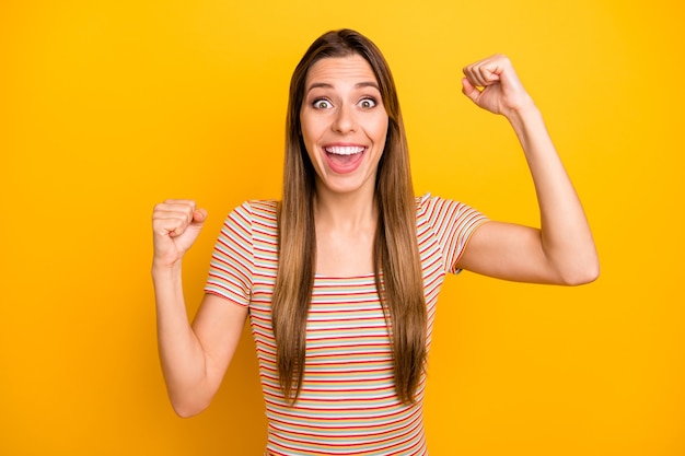 Yeah! Photo of attractive lady yelling loudly unexpected money lottery winning raising hands fists crazy person wear casual striped t-shirt isolated yellow color wall