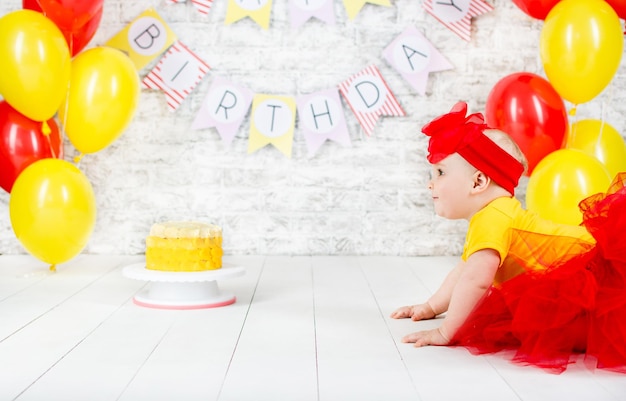 Year-old girl in a blue skirt with a bandage on his head sits near a cream cake pink and blue