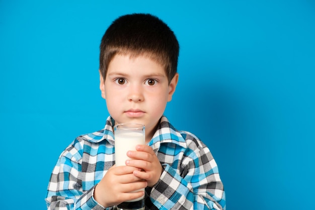 1歳の男の子が青い背景にミルクのガラスを保持します。