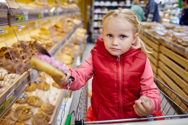 years old girl in shopping cart holds donute in marketplace