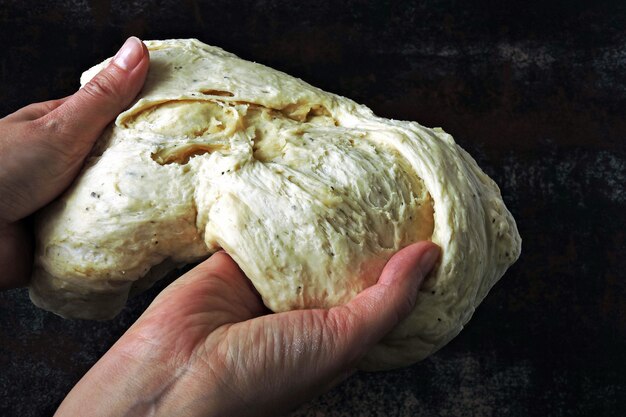 Yeast dough in female hands on a dark background.