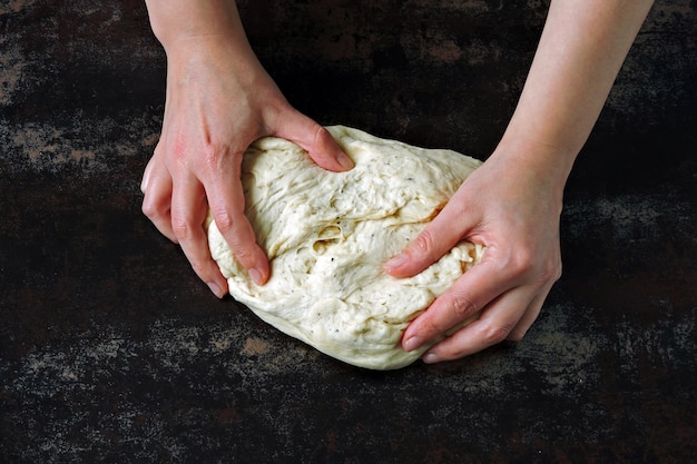 Yeast dough in female hands on a dark background.