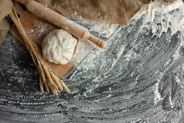 Foto pasta lievitata in tavola con mattarello e spighe di grano. farina sparsa sul tavolo.