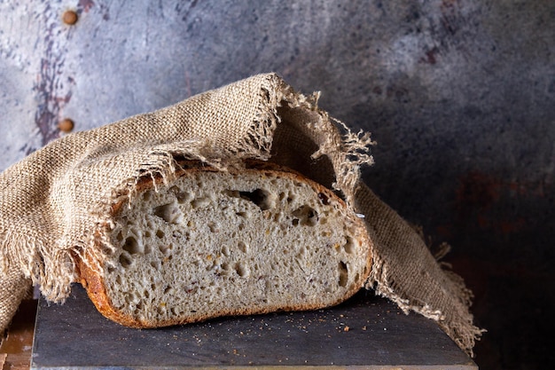 Бездрожжевой хлеб со злаками на деревянной доске, накрытый грубой льняной салфеткой