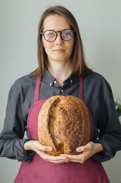 イーストフリーのサワードウパン美しいヨーロッパの女性パン屋が彼女の手にパンを持っています