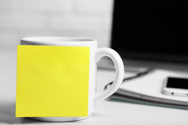 Желтая клейкая записка на кофейной чашке на фоне ноутбука