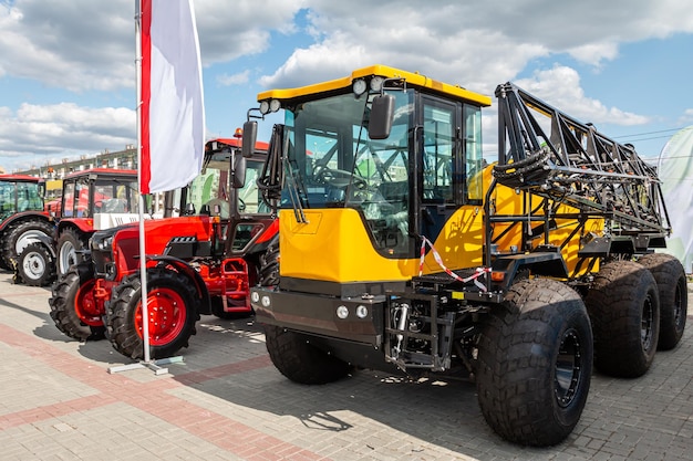 Yellow agricultural all-terrain vehicle with field spraying equipment and red wheeled tractors