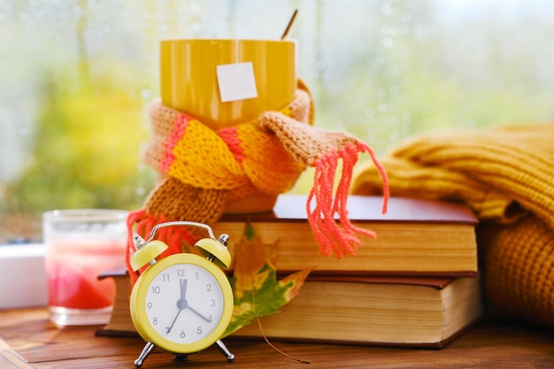 Yellow alarm clock cup on books near the window it's raining