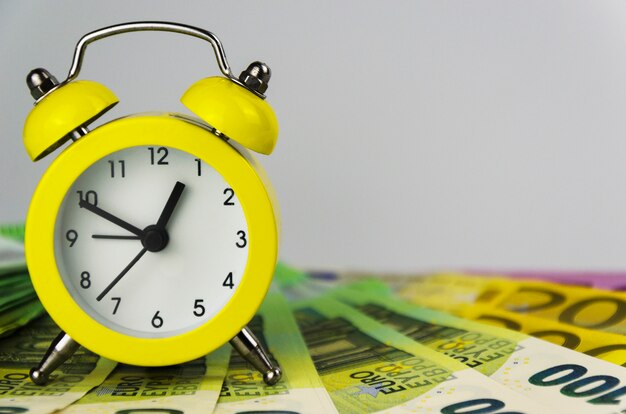 Photo yellow alarm clock and euro banknotes of different denominations