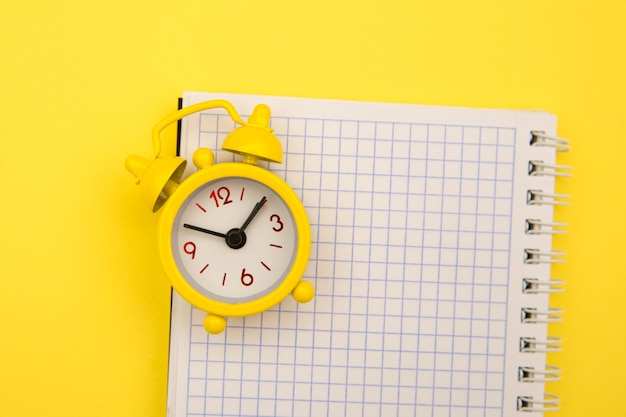 Yellow alarm clock and notebook on yellow