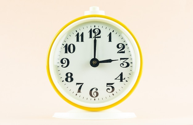 Yellow alarm clock shows the time 15 o'clock on a light isolated background