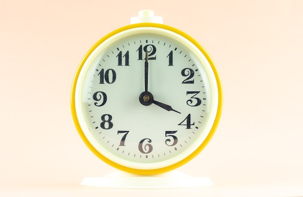 Yellow alarm clock shows the time 16 o'clock on a light isolated background