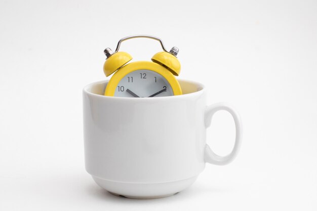 Photo yellow alarm clock in white cup for coffee. early morning time.