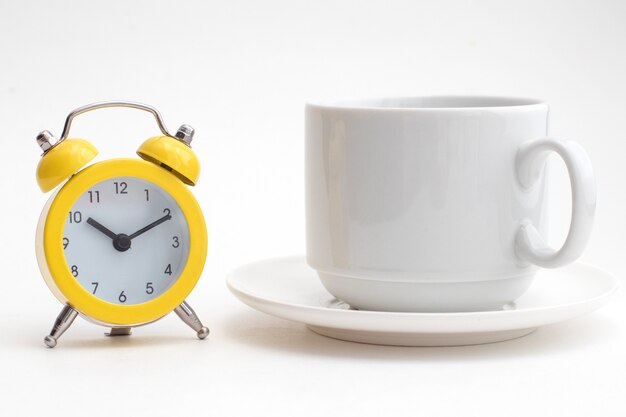 Yellow alarm clock and a white cup of coffee.