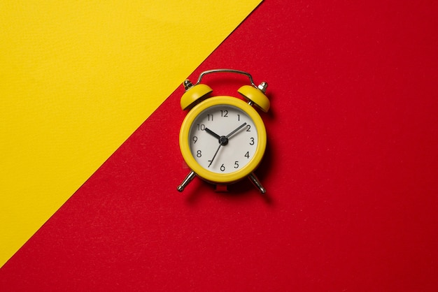 Желтый будильник на желтом, синем, красном и зеленом фоне. Скопируйте пространство. Концепция времени.