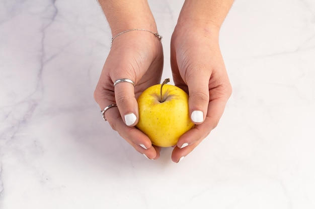 Yellow apple in hands on a marble surface