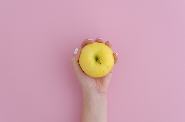 A yellow apple in a lady's hand on pink