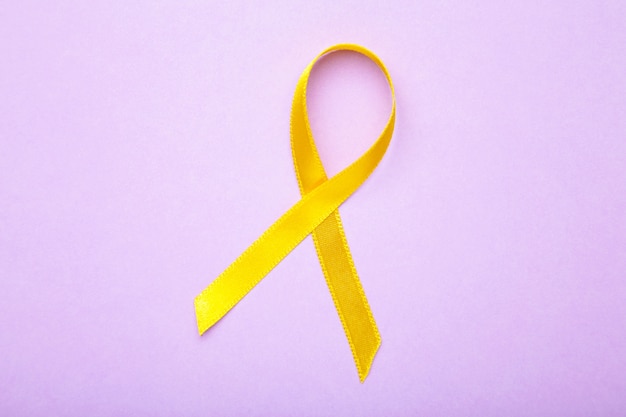 Yellow awareness ribbon on purple surface