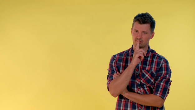 On yellow background cheerful tall boy making a hush gesture it must be quite there