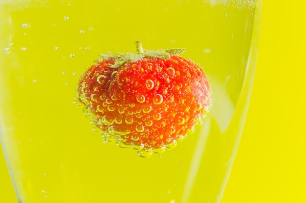 On a yellow background strawberries in a glass with bubbles.