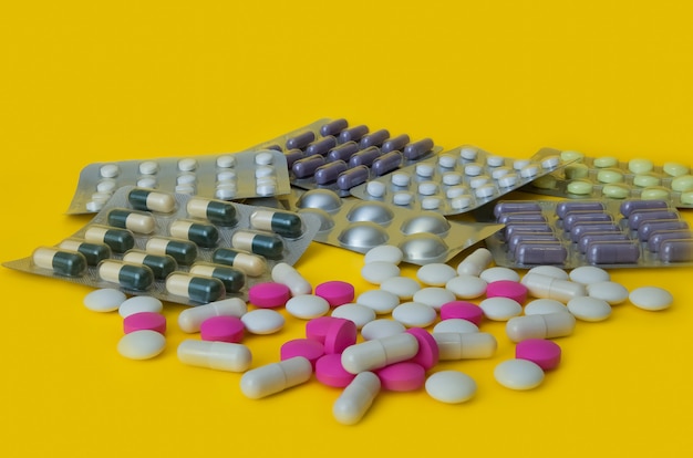 On a yellow background white and pink tablets and blisters with colorful pills are scattered.