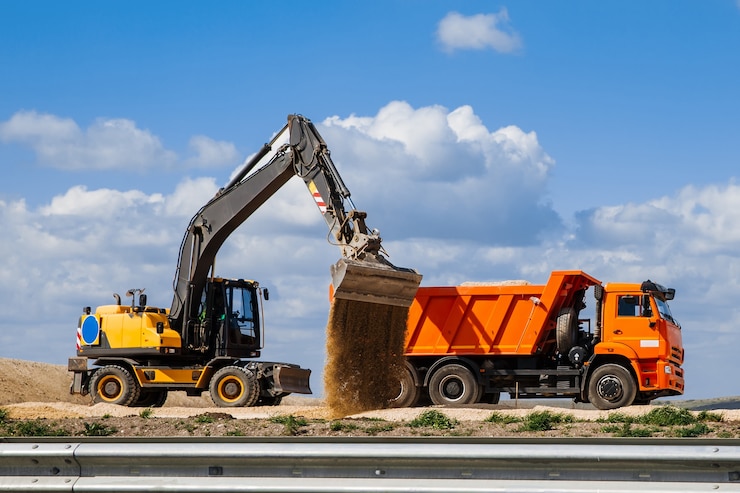 Photo yellow backhoe loader loads the earth into a truck against the sky