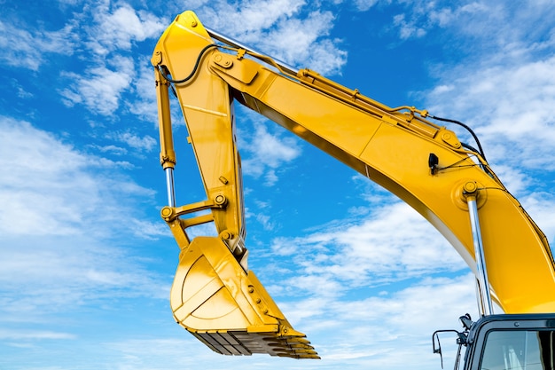 Yellow backhoe with hydraulic piston arm against blue sky. Heavy machine for excavation in construction site. Hydraulic machinery. Huge bulldozer. Heavy machine industry.