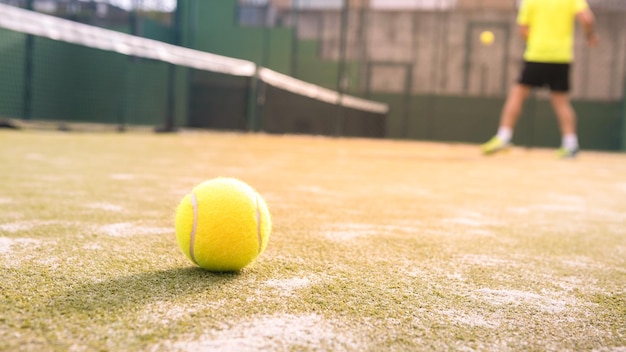 Yellow ball on floor behind paddle net in green court outdoors Padel tennis