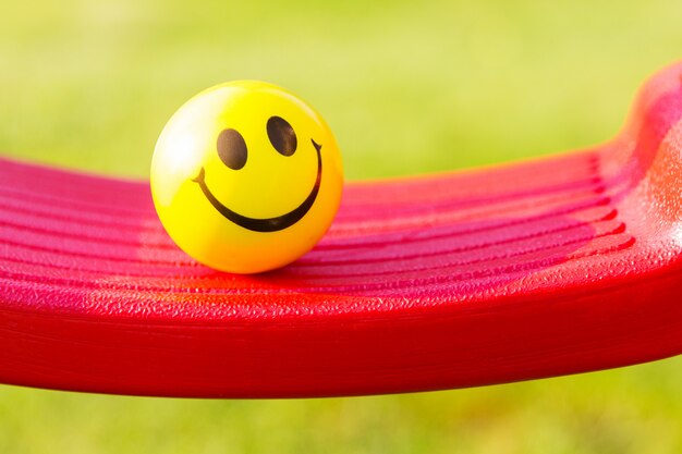 Photo yellow ball with smiling faceon plastic swing on green background