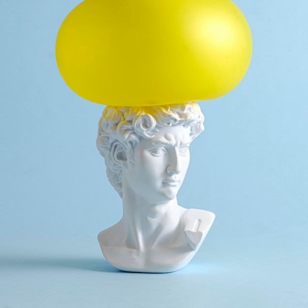 A yellow balloon presses on the head of David of an antique renaissance statue on a pastel blue background as a concept of pressure and problems