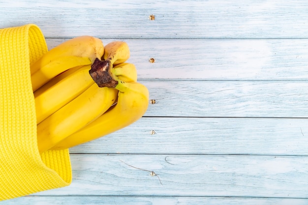 Yellow bananas lying in a yellow bag on a blue wooden background