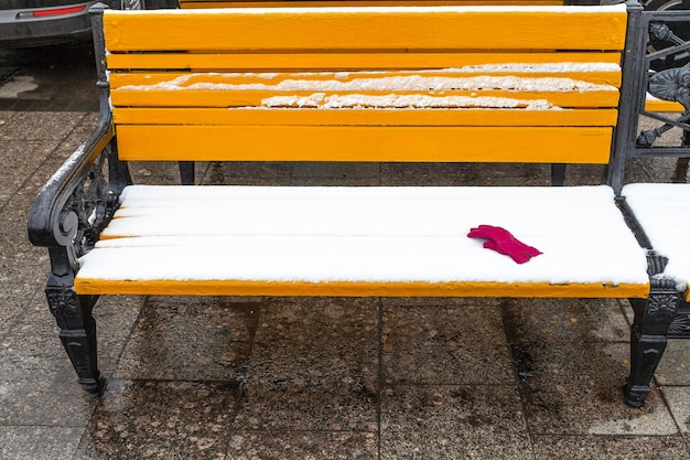 Yellow bench covered by snow with red female glove