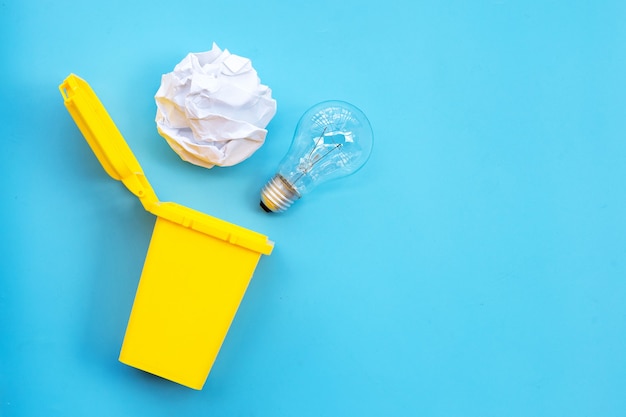 Yellow bin with light bulb and white crumpled paper on blue