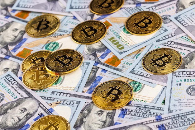 Yellow bitcoin coins scattered over US dollar paper banknotes cryptocurrency and fiat money exchange concept closeup with selective focus