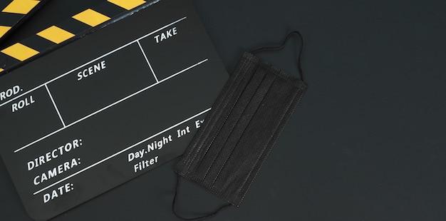 yellow and black clapperboard or movie slate with black face mask  isolated on black background