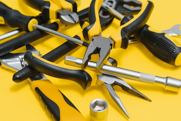 Yellow and black handy tools (pilers and screwdriver) isolated on yellow background