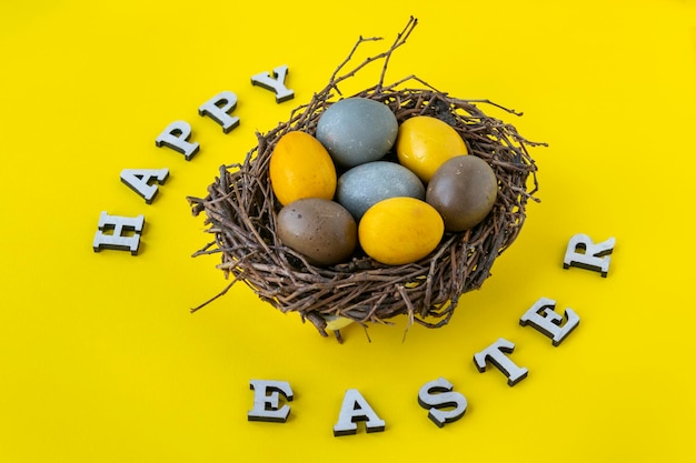 Yellow blue and brown Easter eggs in birds nest on yellow background Happy easter lettering