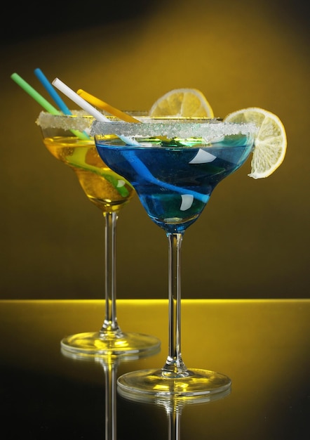 Yellow and blue cocktails in glasses on color background