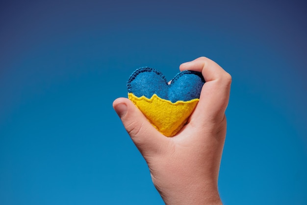 A yellow-blue heart in the hands of a child. against the background of the blue sky. flag of ukraine