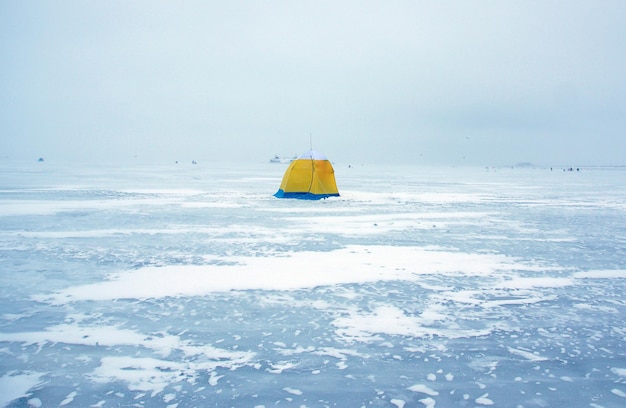 A yellow and blue tent stands in the middle of the bay on thick ice.