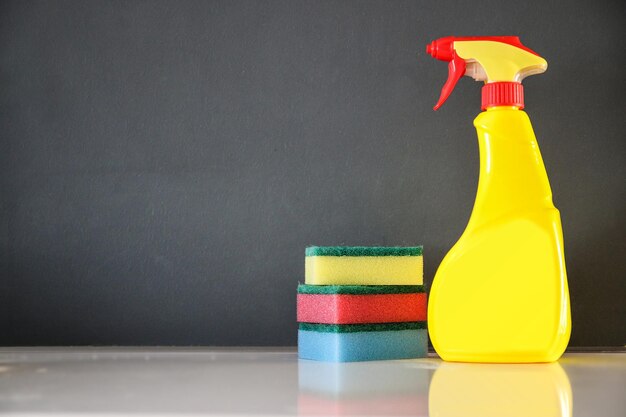 Photo a yellow bottle of cleaning supplies sits next to a stack of sponges.