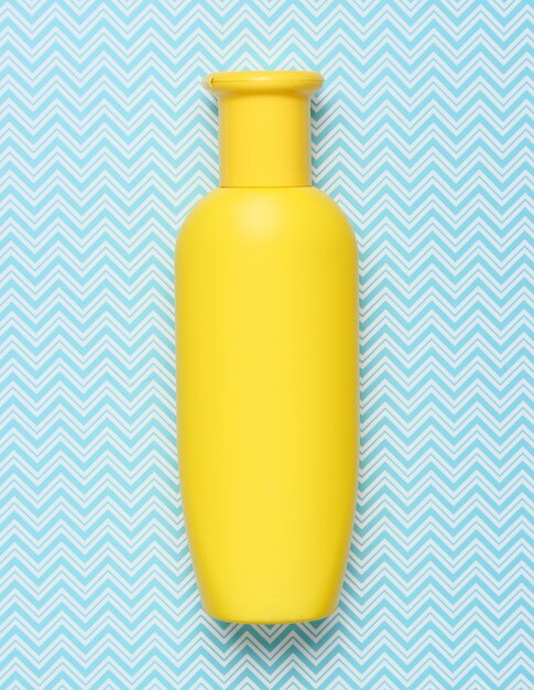 Yellow bottle of shampoo on creative blue, top view