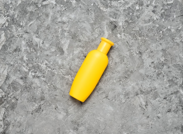 A yellow bottle of shampoo on a gray concrete table. Trend of minimalism. Top view. Products for the shower. Space for text.