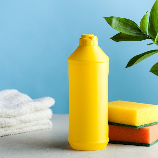 Yellow bottle with place for logo, text with dishwashing liquid, sponges on a blue surface