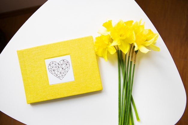 Yellow bouquet of daffodils and yellow book on white table