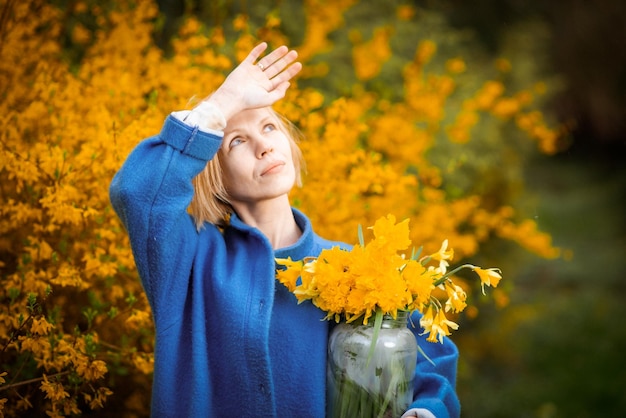 女性の手の中の黄色の花の背景に黄色の花の花束 青いコートを着た中年女性