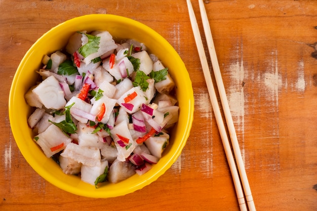 A yellow bowl with ceviche on a wooden table.