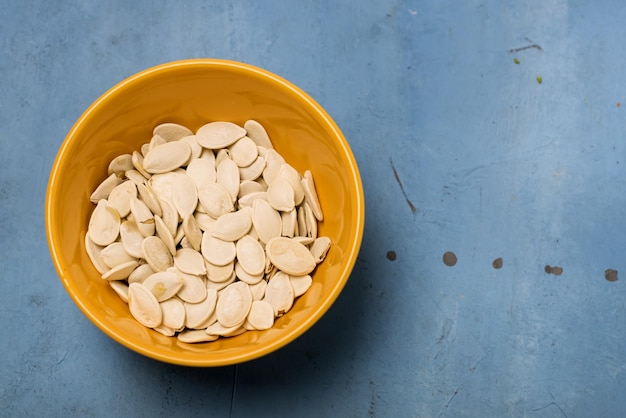 Yellow Bowl with Salted Pumpkin Seeds on Blue Background Copy Space